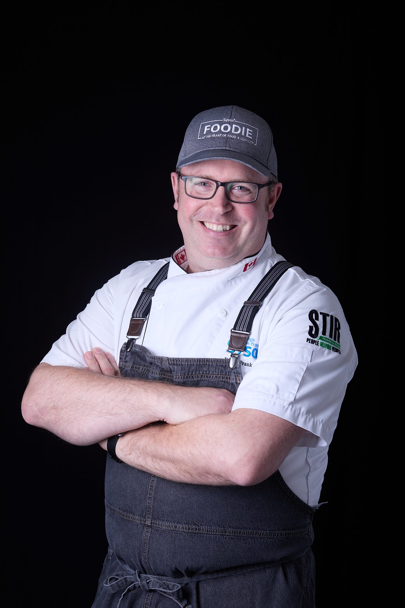 Smiling chef in apron and cap, arms crossed, on black