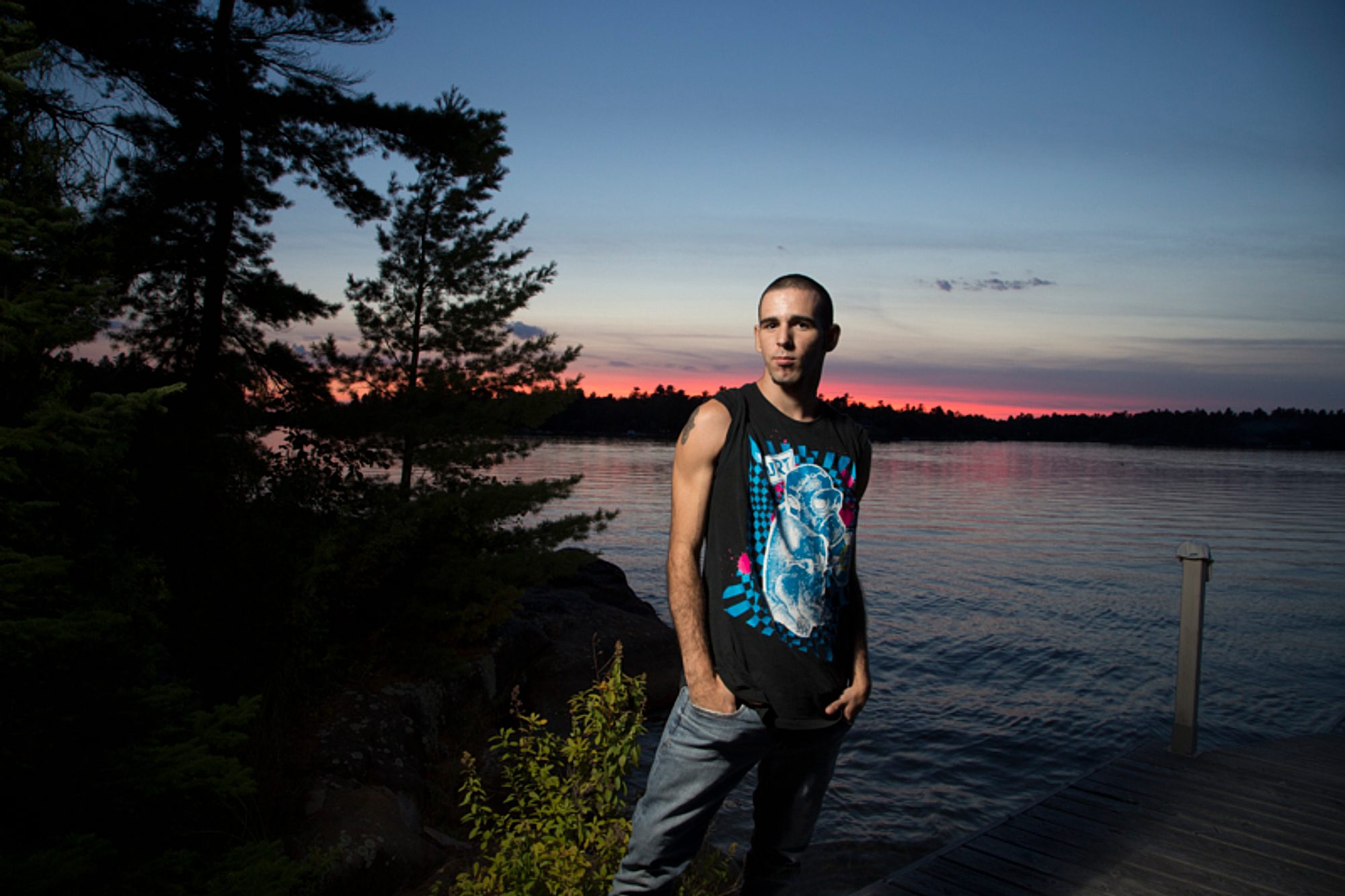 Man on a rocky lakeshore at sunset, lit by flash