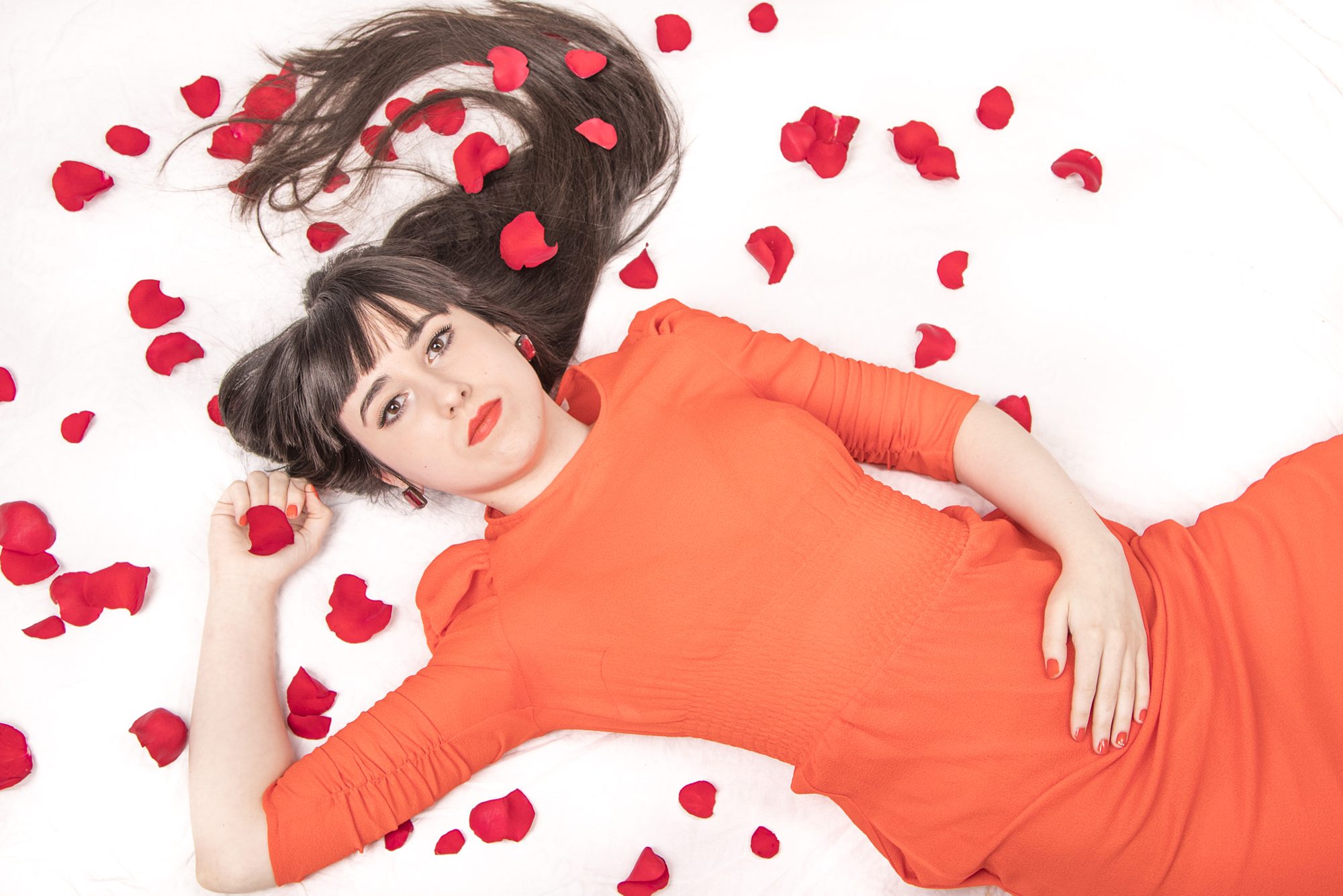 Woman in orange dress lying among rose petals